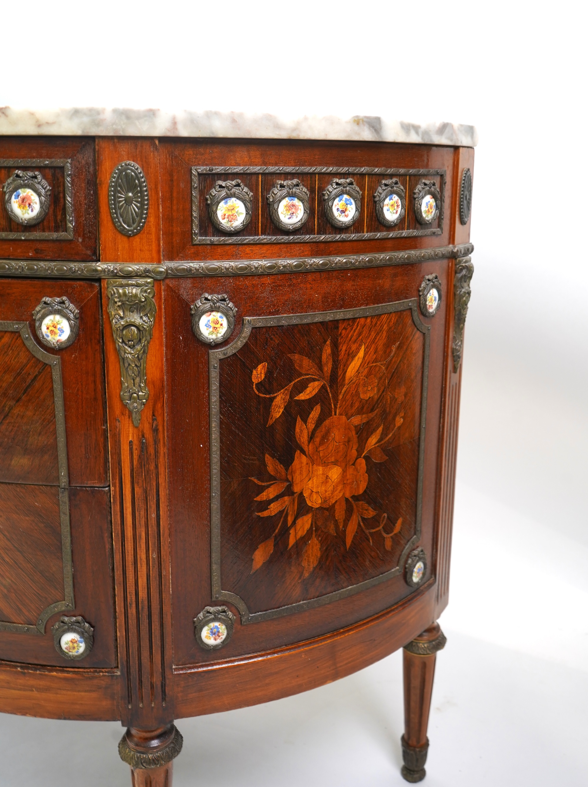 A pair of early 20th century French marquetry inlaid, gilt metal and porcelain mounted rosewood and beech demi-lune commodes
